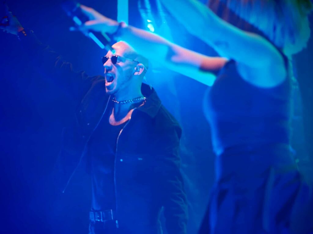 Baptiste de Jive Me chante les bras levés pendant un concert de festival, lumière bleue