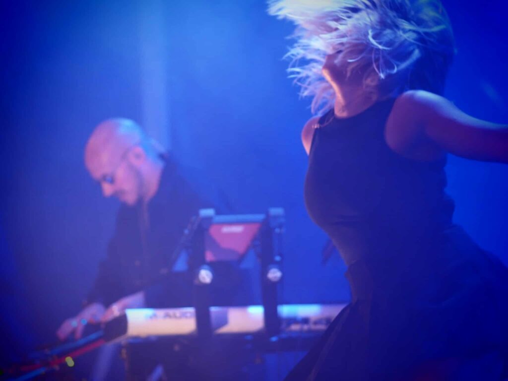 Tara de Jive Me, cheveux en mouvement, danse sur scène en lumière bleue pendant un festival