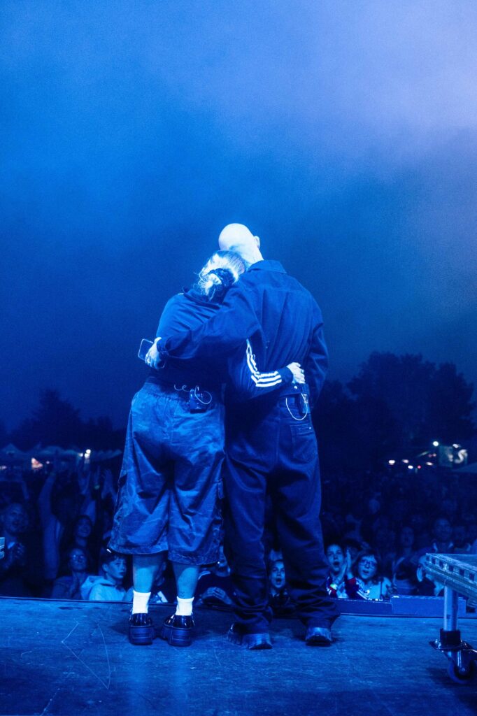 Baptiste et Tara de Jive Me enlacés sur scène, de dos, devant la foule d'un festival